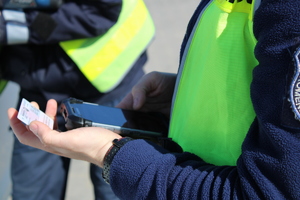 Zdjęcie kolorowe. Policjant trzyma dowód osobisty w ręku podczas sprawdzania w policyjnym systemie