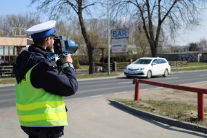 Zdjęcie kolorowe. Policjant dokonuje pomiaru prędkości