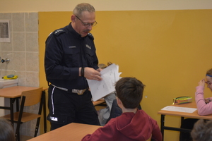 Zdjęcie kolorowe. Policjant wręcza uczniowi test