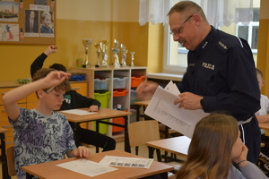 Zdjęcie kolorowe. Policjant wręcza uczniowi test