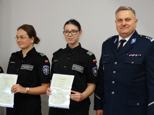 Zdjęcie kolorowe.  Z lewej strony stoją dwie uczennice w umundurowaniu policyjnym obok stoi komendant powiatowy policji ze Szczecinka