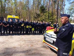 Zdjęcie kolorowe. Na pierwszym planie stoi umundurowany policjant. Za nim w dwuszeregu stoją umundurowani policjanci biorący udział w szkoleniu