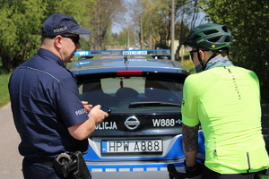 Zdjęcie kolorowe. Policjant rozmawia z rowerzystą na tle radiowozu