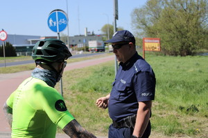 Zdjęcie kolorowe. Policjant rozmawia z rowerzystą w seledynowej koszulce