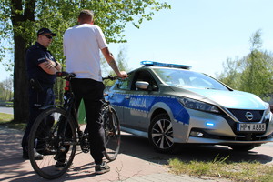 Zdjęcie kolorowe. Policjant rozmawia z rowerzystą