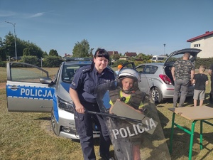 Zdjęcie kolorowe. Policjantka pozuje do zdjęcia z ubranym w sprzęt podwyższonego zagrożenia chłopcem