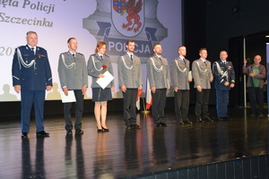 Zdjęcie kolorowe. Na scenie stoi 6 policjantów, którzy otrzymali awans na wyższe stopnie policyjne. Na scenie do szeregu dołączyli komendanci.