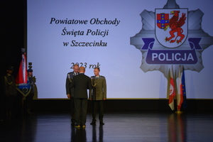 Zdjęcie kolorowe. Starosta szczecinecki wręcza na scenie vouchery wyróżnionym policjantom