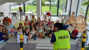 Zdjęcie kolorowe. Policjantka odwrócona plecami rozmawia z dziećmi , które siedzą na dywanie