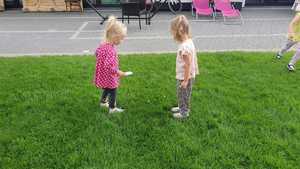 Zdjęcie kolorowe. Dzieci patrząc na trawę przez szkiełko powiększające szukają owadów
