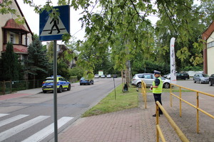 Zdjęcie kolorowe. Policjantka stoi w pobliżu przejścia dla pieszych