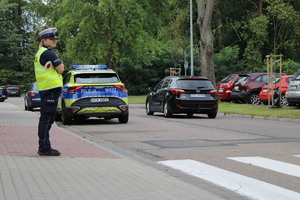 Zdjęcie kolorowe. Policjantka stoi w pobliżu przejścia dla pieszych.