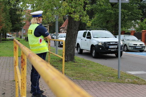 Zdjęcie kolorowe. Policjantka stoi w pobliżu przejścia dla pieszych.