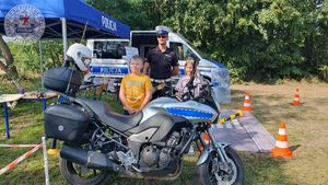 Zdjęcie kolorowe. Policjant asekuruje dziecko na policyjnym motocyklu