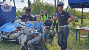 Zdjęcie kolorowe. Policjant asekuruje dziecko na policyjnym motocyklu