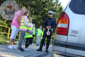 Zdjęcie kolorowe. Policjant w obecności dzieci prowadzi kontrolę drogową