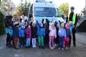 Zdjęcie kolorowe. Na tle busa wspólne zdjęcie przedszkolaków z policjantem