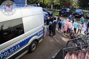 Zdjęcie kolorowe. Z lewej strony stoi policyjny bus, z prawej strony zgromadzone są dzieci