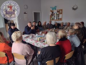 Zdjęcie kolorowe. Przy wspólnym dużym stole siedzą seniorzy oraz umundurowani policjanci