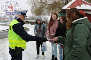 Zdjęcie kolorowe. Policjant wręcza elementy odblaskowe przechodniom