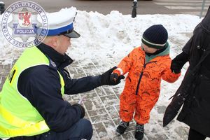 Zdjęcie kolorowe. Policjant wręcza elementy odblaskowe przechodniom