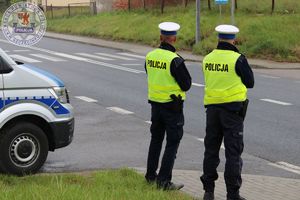 Zdjęcie kolorowe. Policjanci obserwują przy radiowozie ruch na drodze