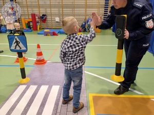 Zdjęcie kolorowe. Policjantka na macie z przejściem dla pieszych ćwiczy z dziećmi