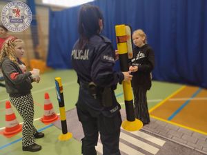 Zdjęcie kolorowe. Policjantka na macie z przejściem dla pieszych ćwiczy z dziećmi