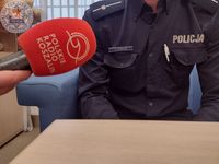 Zdjęcie kolorowe. Mikrofon koloru czerwonego z napisem Polskie Radio Koszalin, w tle policyjny mundur.