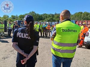 Zdjęcie kolorowe. Odwrócona plecami policjantka stoi obok mężczyzny w kamizelce odblaskowej z napisem budimex