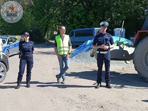 Zdjęcie kolorowe. Policjanci stoją na tle maszyn budowlanych. Pomiędzy nimi mężczyzna w  kamizelce odblaskowej