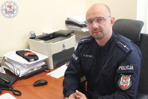 Zdjęcie kolorowe. Policjant siedzący przy biurku