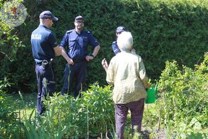 Zdjęcie kolorowe. Policjanci rozmawiają z działkowiczami