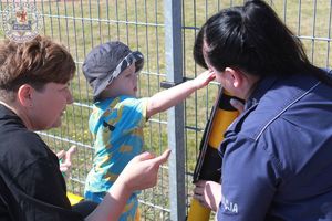 Zdjęcie kolorowe. Policjantka ćwiczy z dziećmi przechodzenie przez przejście dla pieszych