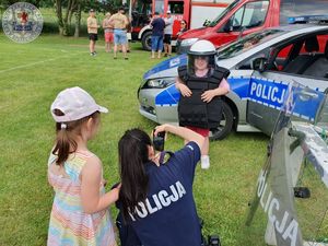 Zdjęcie kolorowe. Policjantka robi zdjęcie dziecku ubranemu w strój podwyższonego ryzyka