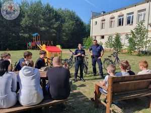 Zdjęcie kolorowe. Policjanci stoją przed grupą uczniów. U ich boku stoją rowery