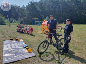 Zdjęcie kolorowe. Policjanci stoją przed grupą uczniów. U ich boku stoją rowery