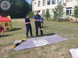 Zdjęcie kolorowe. Policjanci na terenach zielonych przy szkole prowadzą spotkanie z uczniami