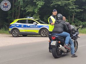 Zdjęcie kolorowe. Policjant kontroluje motocyklistę