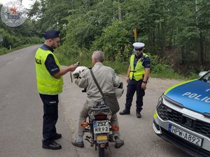 Zdjęcie kolorowe. Policjant kontroluje motocyklistę