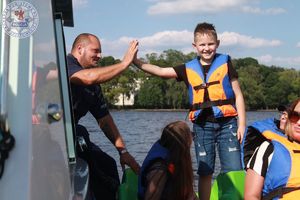 Zdjęcie kolorowe. Podczas kontroli osób pływających na rowerze wodnym policjant przebija piątkę chłopcu