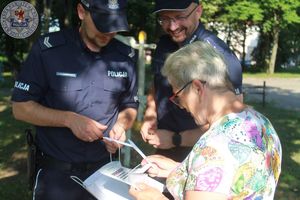 Zdjęcie kolorowe. Policjanci rozmawiają z kobietą