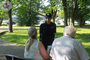 Zdjęcie kolorowe. Policjantka rozmawia z parą seniorów siedzących na ławce w parku
