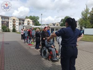 Zdjęcie kolorowe. W parach grupa dzieci i młodzieży porusza idzie za policjantką