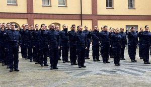 Zdjęcie kolorowe. Na dziedzińcu policjanci stoją na baczność tworząc pododdział