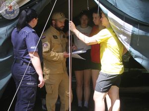 Zdjęcie kolorowe. Policjantka strażak i komendantka obozu rozmawiają w namiocie