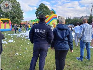 Zdjęcie kolor. Odwrócona plecami policjantka i przedstawicielka sanepidu patrzą na bawiące się dzieci w pianie