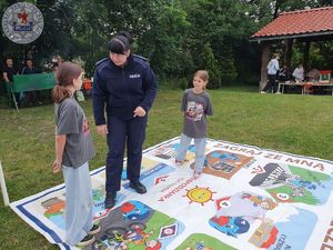 Zdjęcie kolorowe. Policjantka gra z dziećmi w wielkoformatową grę planszową