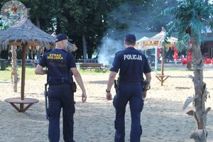 Zdjęcie kolorowe. Policjant i strażnik patroluje kąpielisko i plażę