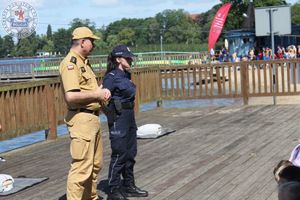 Zdjęcie kolorowe. Strażak i policjantka stoją przed liczną grupą dzieci